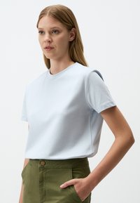 T-shirt di cotone azzurro chiaro con maniche corte, scollo rotondo e vestibilità rilassata. Abbinato a pantaloni verde oliva con tasca frontale.