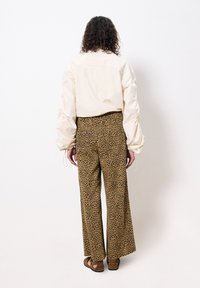 Chemise beige surdimensionnée avec des manches froncées, associée à un pantalon large en imprimé léopard marron. Des sandales marron viennent compléter la tenue.
