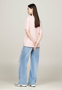 Camiseta de manga corta rosa claro combinada con unos vaqueros de corte holgado en azul claro. Los vaqueros presentan un ligero efecto desgastado.