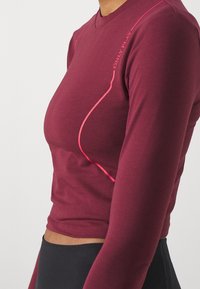 Maglietta a maniche lunghe in tessuto bordeaux con linee di accento rosa; presenta un collo a V e un design aderente che mette in risalto la silhouette di chi la indossa.
