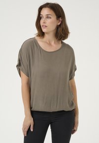 Top corto e morbido di colore verde oliva, con maniche corte e scollatura tonda, realizzato in un tessuto morbido e testurizzato. Abbinato a jeans neri aderenti.