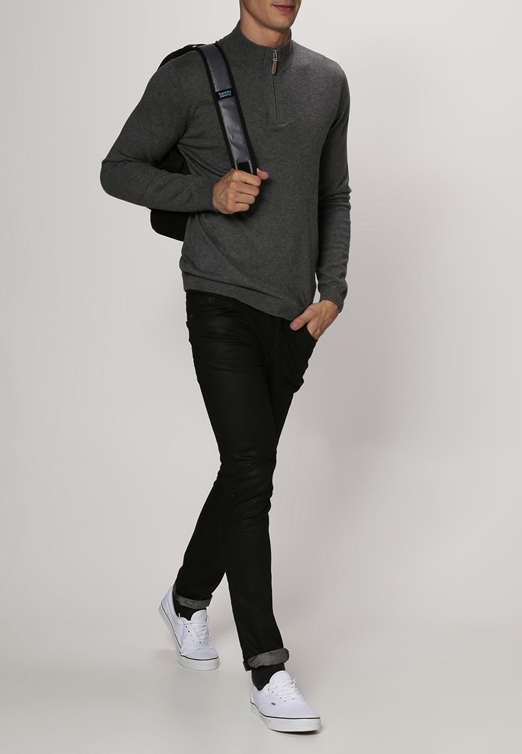 Homme marchant portant un pull gris à fermeture éclair au quart, pantalon noir, baskets blanches et portant un sac à bandoulière noir.