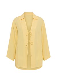 Κίτρινη, ελαφριά μπλούζα με γιακά, ανοιχτό μπροστινό μέρος και δύο κορδόνια μπροστά. Διαθέτει μακριά, φαρδιά μανίκια και άνετη  εφαρμογή.