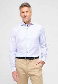 Camicia azzurro chiaro a maniche lunghe con un motivo testurizzato, caratterizzata da bottoni scuri e colletto a punta, abbinata a pantaloni beige.