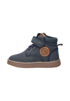 Bota azul oscura con una correa de velcro y cordones, que presenta un parche con un logo circular y una suela de goma marrón. Material suave con un acabado texturizado.