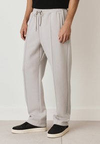 Light grey jogger pants made of soft fabric, featuring a drawstring waistband, side pockets, and contrasting stitching details.