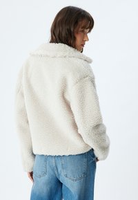 Hvid faux shearling jakke med krave, cropped design og afslappet pasform. Sammen med lyseblå denim jeans.