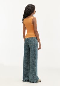 Oversized orange ærmeløs tanktop parret med brede blå leopardmønstrede jeans. Struktureret stof og diskrete detaljer på buksernes lommer.