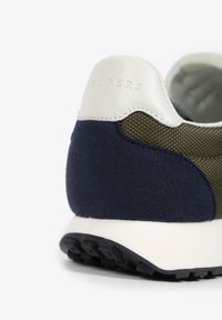 Sneaker met een combinatie van olijfgroene stof, marineblauwe suede en witte leren accenten. Voorzien van een gestructureerde hak en een zwarte rubberen zool.