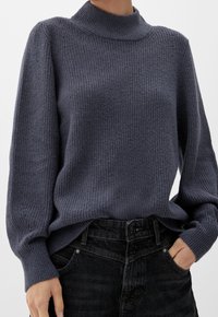 Dunkelgrauer, gestrickter Pullover mit hohem Kragen, gerippter Textur und langen Ärmeln, kombiniert mit schwarzen, hoch taillierten Jeans.