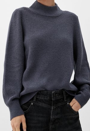 Sweter w ciemnoszarym kolorze, dziany, z wysokim kołnierzem, prążkowaną fakturą i długimi rękawami, zestawiony z czarnymi spodniami dżinsowymi o wysokim stanie.