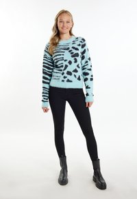 Pulover pufoș albastru deschis cu pete și dungi negre de leopard; guler rotund; manșete și tiv cu bordură; asortat cu blugi skinny negri și cizme negre.