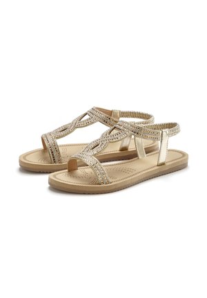 Beige flache Sandalen mit elastischem Knöchelriemen, mit geflochtenem und mit Strasssteinen verziertem T-Riemen-Design und leicht gepolsterter Sohle.