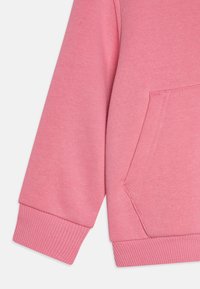 Felpa rosa con tessuto testurizzato, polsini a costine e una tasca frontale con dettagli di cucitura. Evoca un'estetica di design casual.