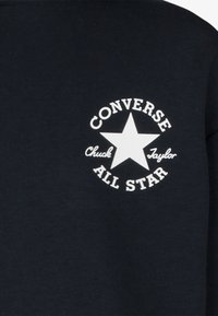 Crna dukserica s bijelim kružnim logom s zvijezdom i natpisom "Converse Chuck Taylor All Star" u podebljanom fontu.