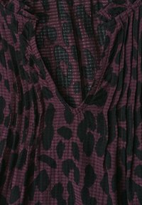 Vêtement à col en V avec une texture plissée et un motif léopard violet foncé et noir sur le tissu.