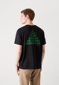 Svart t-skjorte med korte ermer, med et grønt gjentatt tekstdesign på baksiden, rund hals og en avslappet passform.