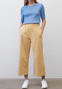 Modrý žebrovaný top s krátkým rukávem v kombinaci se žlutými širokými kalhotami a bílými teniskami. Obsahuje elastický pas a boční kapsy.