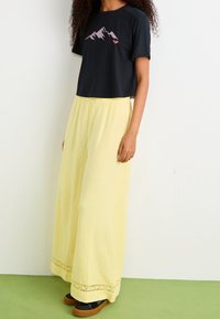 Black cropped t-shirt with mountain graphic, paired with flowing yellow palazzo pants featuring lace trim at the hem. Black and brown shoes.