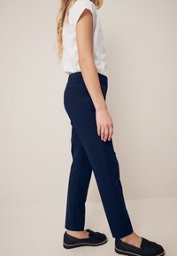 Pantaloni blu tailored con una vestibilità slim, abbinati a una maglietta bianca a maniche corte e mocassini neri. Tessuto morbido con un design classico.