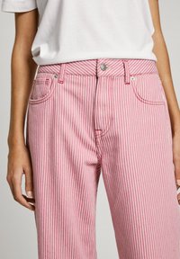 Randiga rosa och vita jeans med femfickorsdesign, knappstängning och lätt textur. Har vit sömnad och metallelement.