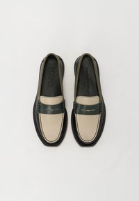 Mocassins avec une tige beige, une bande en cuir vert foncé et une semelle noire. Comprend des coutures contrastées et un logo embossé sur la semelle intérieure.
