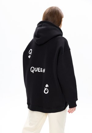 Hoodie noir en tissu doux avec une coupe ample. Présente un texte imprimé blanc "Q" et "QUEEN" ainsi que des éléments graphiques au dos.