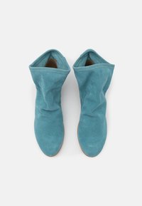 Blå ruskind ankelstøvler med slouchy design, spids tå og glat overflade. Subtil syning langs den øverste åbning. Flad beige sål.