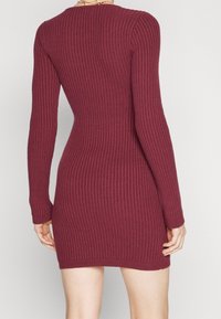 Ribbat, långärmad klänning i bordeaux, med en figurnära silhuett och rund halsringning, som framhäver ett texturerat stickat tyg.