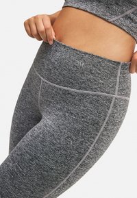Leggings deportivos de alta cintura en un patrón gris texturizado. Presentan costuras en gris claro en contraste y un detalle del logo cerca de la cinturilla.