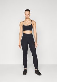 Svart sportsbh og høy midje leggings laget av et elastisk materiale. Antrekket har tynne stropper og en glatt, matt overflate.