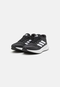 Black athletic shoes with a textured mesh upper, three white stripes on the sides, and a white sole. Rounded toe and lace-up design.