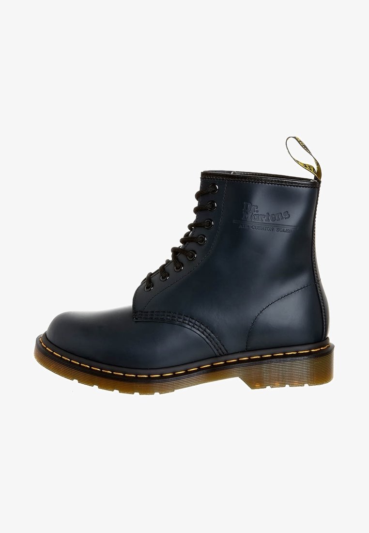Botín negro de cuero hasta el tobillo con punta redonda, ocho ojales, costuras amarillas y bucle para tirar. Suela texturizada para mayor agarre. Branding icónico de Dr. Martens.