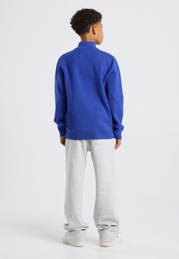 Blauwe pullover met een hoge kraag, grijze sweatpants en witte schoenen. Zachte textuur; casual, relaxte pasvorm; minimalistisch ontwerp zonder patronen.