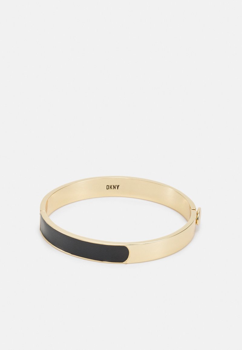 Bracelet jonc ton doré avec un accent en émail noir et "DKNY" gravé sur le côté intérieur, sur fond blanc.