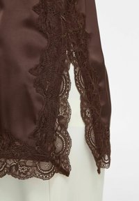 Gros plan sur un tissu en satin marron avec une bordure en dentelle florale délicate le long des bords festonnés et une petite fente à l'avant.