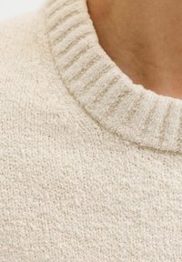 Grietos mezginės vilnos megztinis su raukšlėtu apykaklės kraštu. Audinys turi tekstūrinį, minkštą išvaizdą su subtiliais audimo variacijomis.