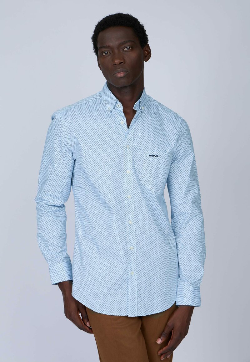 Chemise boutonnée bleu clair avec un motif géométrique, manches longues et col. Présente un petit logo brodé sur la poitrine.