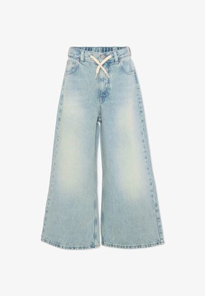 Pantalon en denim bleu clair à jambes larges avec ceinture élastique et cordon blanc, avec des poches avant et un effet délavé sur les cuisses.