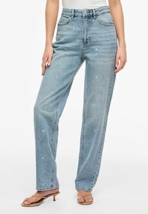 Lyseblå jeans med høj talje med små hvide broderede blomster, båret med tanfarvede sandaletter med hæl.