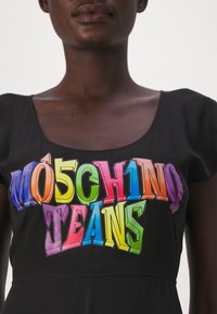 Fekete, rövid ujjas felső, amely színes, merész grafikával rendelkezik, rajta a "MOSCHINO TEANS" felirattal különböző élénk színekben és 3D hatású megjelenéssel.