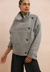 Gray wool-blend pullover with high collar, side buttons, and dropped shoulders. Features a textured finish and relaxed fit.