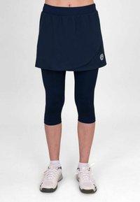 Falda deportiva marinera con cintura elástica, diseño en capas, combinada con leggings marineros. Detalle de zapatillas blancas en los pies, textura de tela suave.