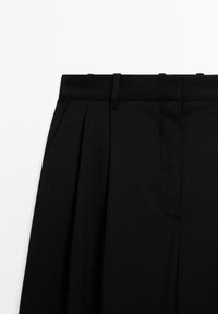 Černé elegantní kalhoty s hladkou texturou, s plochým předním dílem, dvěma sklady, poutky na pásek a bočními kapsami.