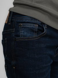 Tmavě modré džínové kalhoty s oranžovým prošíváním, které mají boční kapsu a koženou nášivku značky nad zadní kapsou.