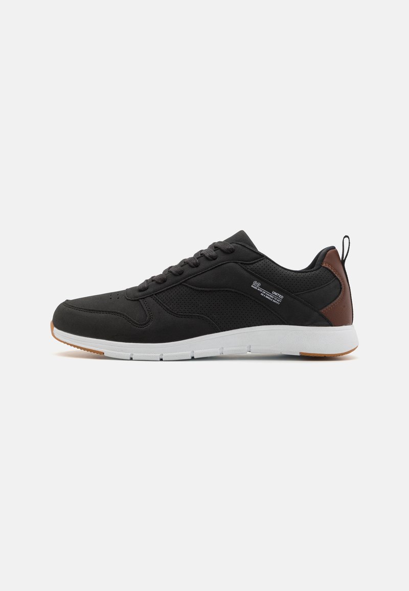 Black athletic shoe with a smooth synthetic upper, perforated detailing, brown leather accent at the heel, and a white rubber outsole.