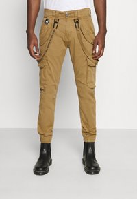 Khaki cargo bukser med flere lommer, justerbare sideløkker, tætsiddende ben og elastiske manchetter, parret med sorte ankelstøvler.