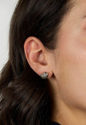 Orecchino a perno a forma di cuore in argento, superficie liscia, finitura riflettente, attaccato all'orecchio, con una vista ravvicinata del lobo dell'orecchio e dei capelli.
