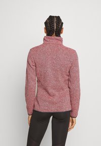 Veste en polaire chinée rouge et blanche avec un col montant et des manches longues, dotée d'une texture douce et d'une silhouette ajustée.