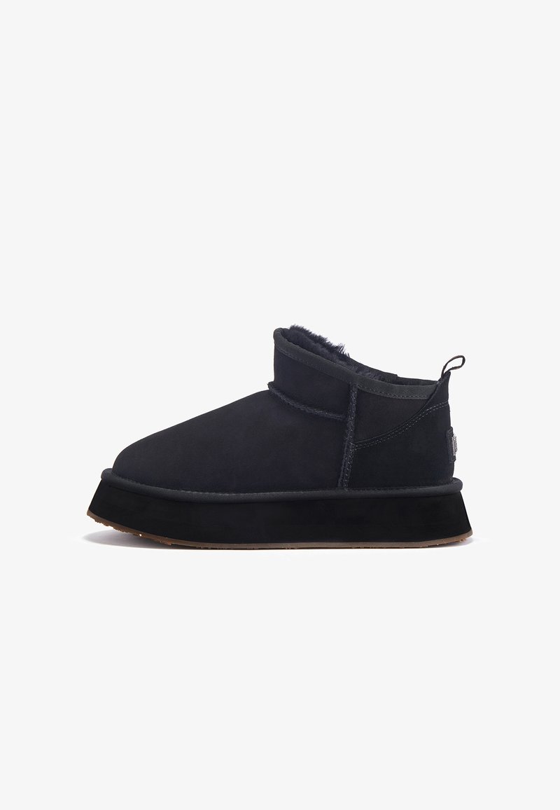Botines de ante negro con un suave forro interior, suela de goma plana y puntera redonda. Presentan un acento acolchado y una lengüeta en el talón para facilitar el calzado.
